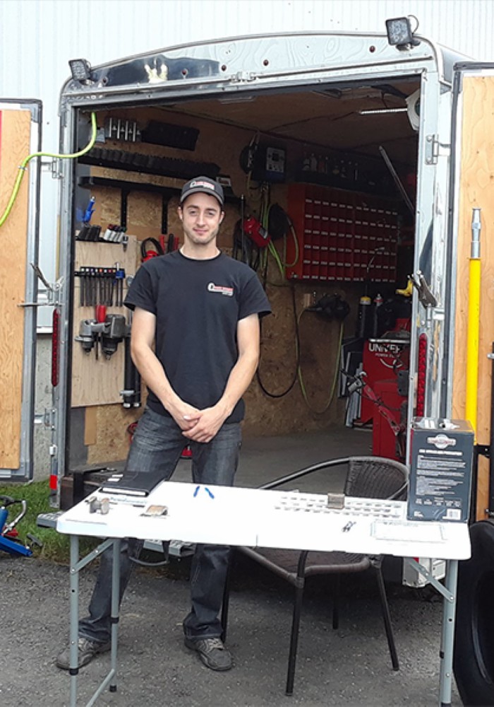 Technicien de Pneu Mobile Rive-Sud posant à côté d'un pneu agricole de grande taille, avec remorque de service mobile en arrière-plan.